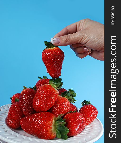 Woman's hand taking strawberry from plate full of fruits. Woman's hand taking strawberry from plate full of fruits