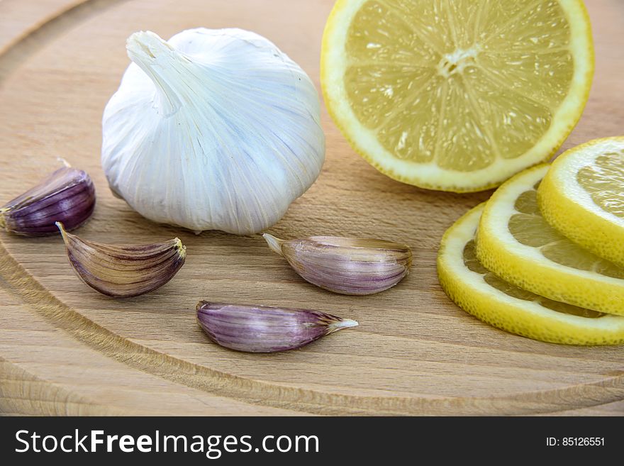 Sliced lemon and whole garlic with cloves on wooden cutting board. Sliced lemon and whole garlic with cloves on wooden cutting board.
