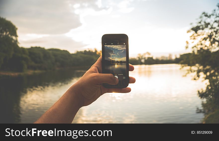 Close-up Of Hand Holding Mobile Phone Against Lake