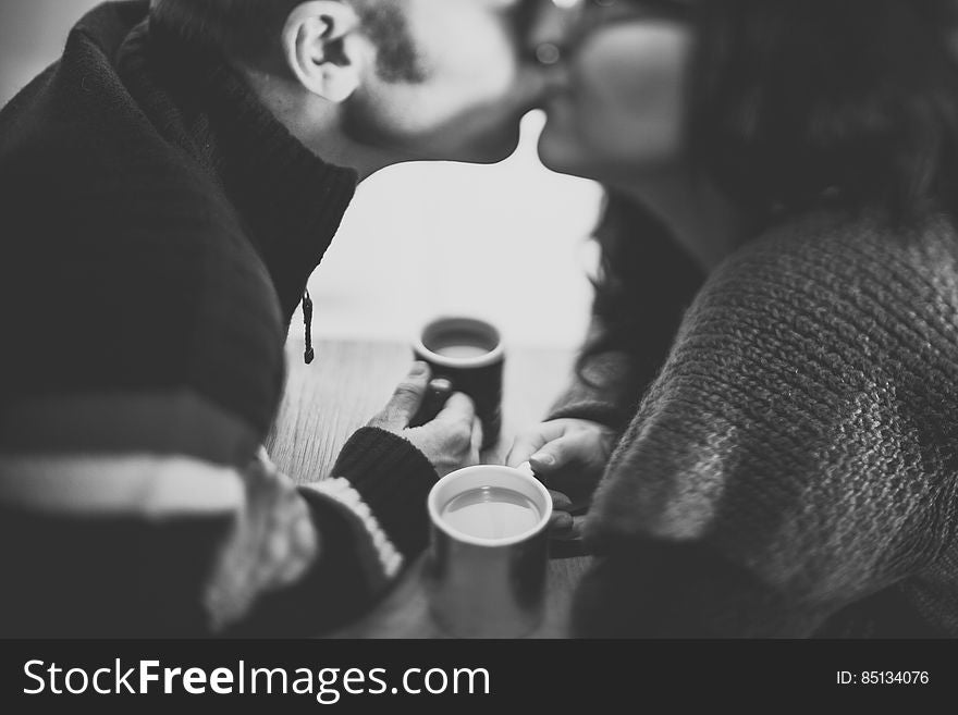 A black and white photo of a couple kissing holding coffee cups. A black and white photo of a couple kissing holding coffee cups.