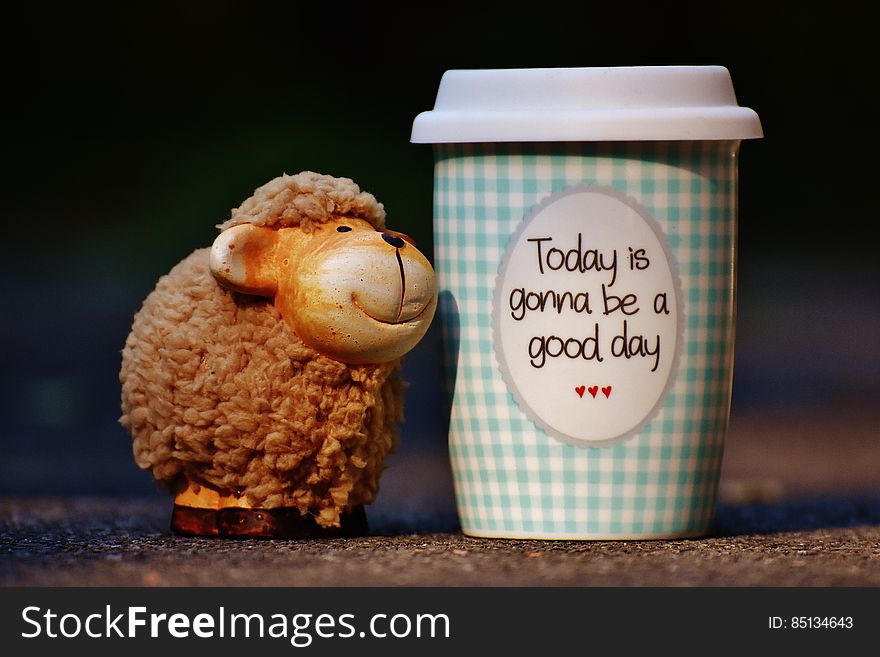 A take-away cup of coffee and a small sheep figure. A take-away cup of coffee and a small sheep figure.