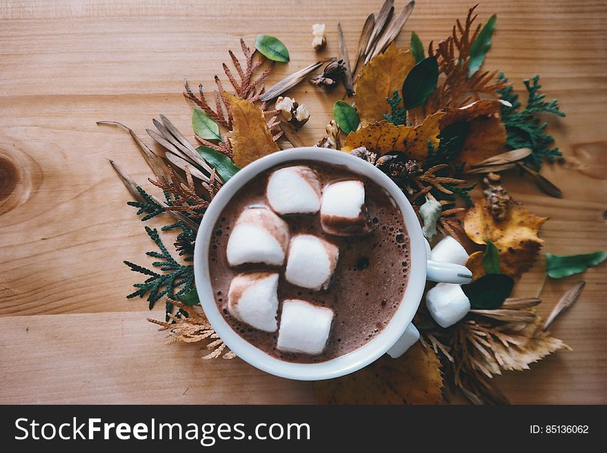 A cup of coffee with marshmallows inside and autumn leaves around as decoration. A cup of coffee with marshmallows inside and autumn leaves around as decoration.
