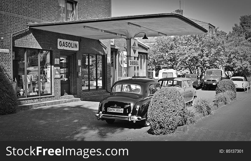 A black and white old fashioned gas station and vintage cars.