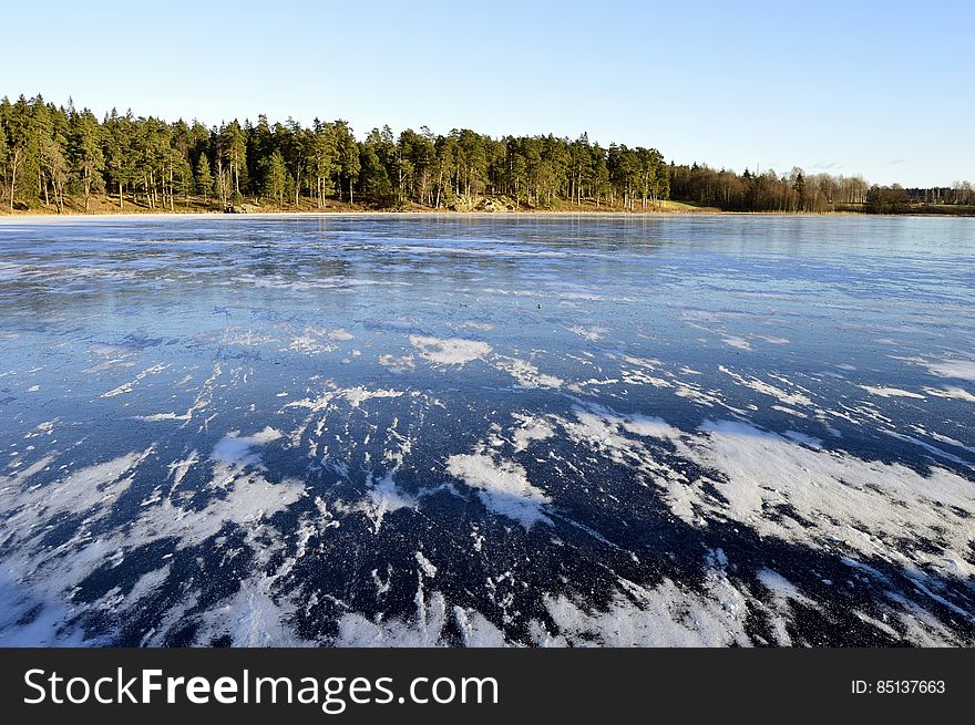 Swedish lake with white foam on blue waters and beyond it dense forest, pale blue sky. Swedish lake with white foam on blue waters and beyond it dense forest, pale blue sky.