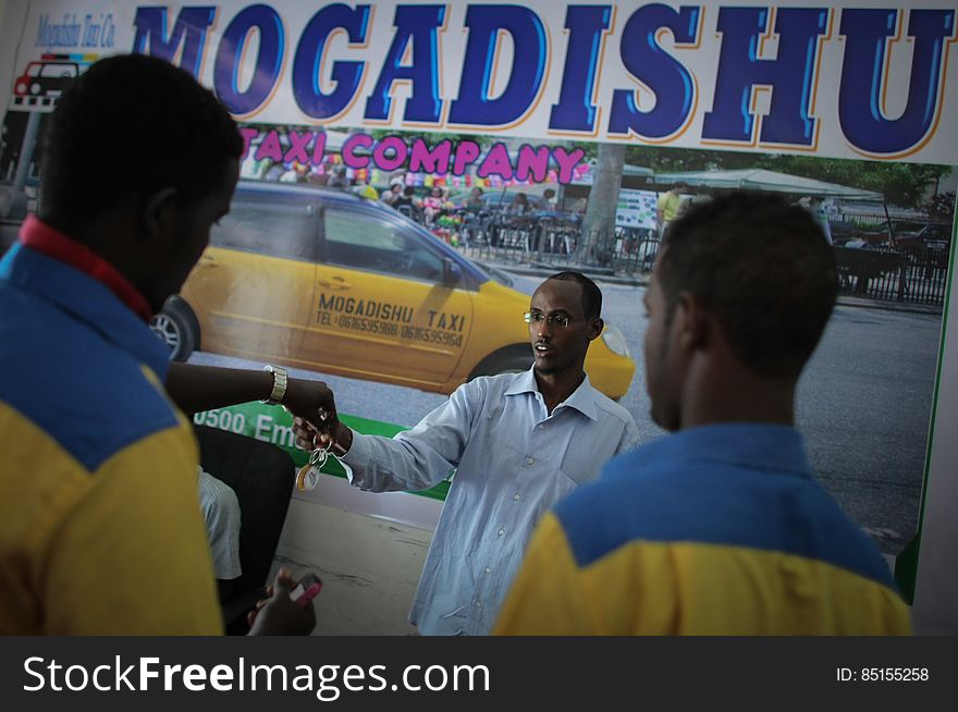 Suleiman Mohamed Daras &#x28;centre&#x29;, manager of the Mogadishu Taxi Company hands a set f keys to one of his drivers at the company&#x27;s head office in the Somali capital Mogadishu, 01 September 2013. Operating since the end of May of this year in the city&#x27;s dusty and once again bustling streets and thoroughfares, the MTC&#x27;s distinctive yellow and purple cars offer customers taxi fares around Mogadishu at competitive rates and in the first 3 months of operations, the company has increased it&#x27;s fleet of vehicles from an initial 25 to over 100. The company, according to one of it&#x27;s drivers, also enables employment opportunities for Somalia&#x27;s youth following two decades of conflict in the Horn of Africa nation that shattered a generation. Now, thanks to the relative peace that has followed the departure of the Al-Qaeda-affiliated extremist group Al Shabaab from the city; an internationally recognised government for the first time in years and thousands of Diaspora Somalis returning home to invest in and rebuild their country, the MTC is one of many new companies establishing itself in the new Mogadishu and offering services that were hitherto impossible to provide. AU-UN IST PHOTO / STUART PRICE. Suleiman Mohamed Daras &#x28;centre&#x29;, manager of the Mogadishu Taxi Company hands a set f keys to one of his drivers at the company&#x27;s head office in the Somali capital Mogadishu, 01 September 2013. Operating since the end of May of this year in the city&#x27;s dusty and once again bustling streets and thoroughfares, the MTC&#x27;s distinctive yellow and purple cars offer customers taxi fares around Mogadishu at competitive rates and in the first 3 months of operations, the company has increased it&#x27;s fleet of vehicles from an initial 25 to over 100. The company, according to one of it&#x27;s drivers, also enables employment opportunities for Somalia&#x27;s youth following two decades of conflict in the Horn of Africa nation that shattered a generation. Now, thanks to the relative peace that has followed the departure of the Al-Qaeda-affiliated extremist group Al Shabaab from the city; an internationally recognised government for the first time in years and thousands of Diaspora Somalis returning home to invest in and rebuild their country, the MTC is one of many new companies establishing itself in the new Mogadishu and offering services that were hitherto impossible to provide. AU-UN IST PHOTO / STUART PRICE.