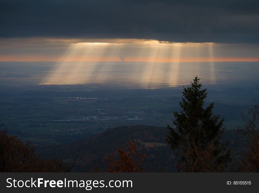 Sun beams over landscape from behind clouds at sunrise.