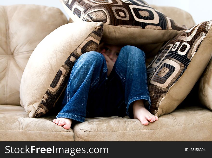 Young boy wearing blue jeans hiding in cushion tent on couch. Young boy wearing blue jeans hiding in cushion tent on couch.