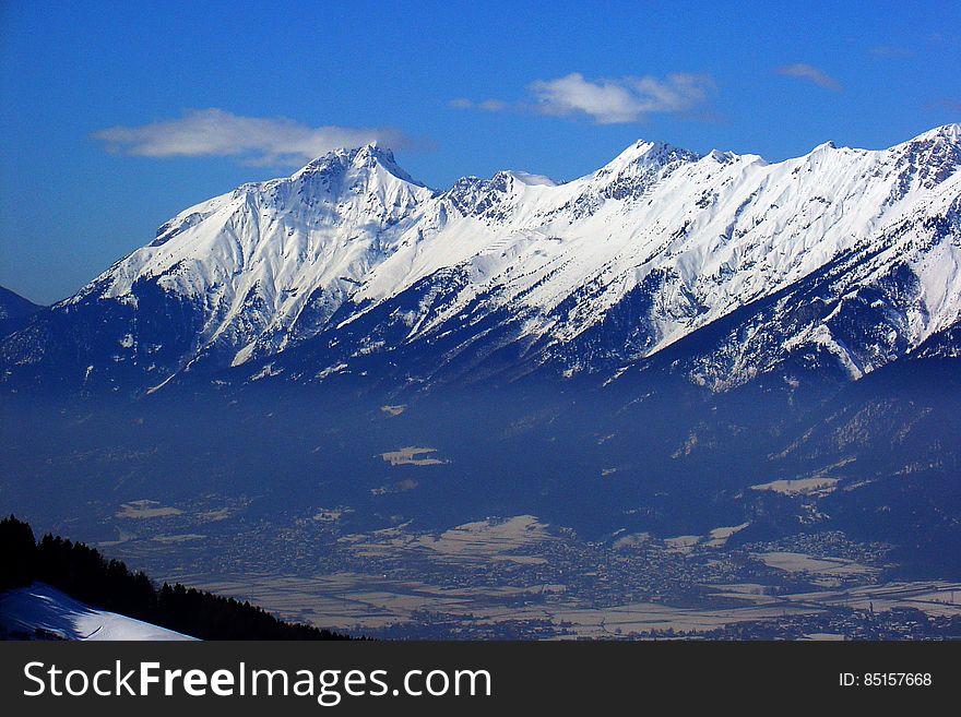 Landscape of snow capped mountain peaks and valley against blue skies on sunny day.