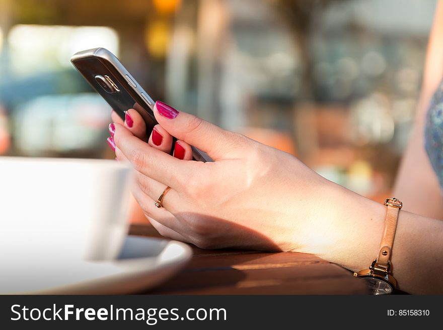 Person Holding a Black Smartphone Wearing a Brown Leather Strap Watch