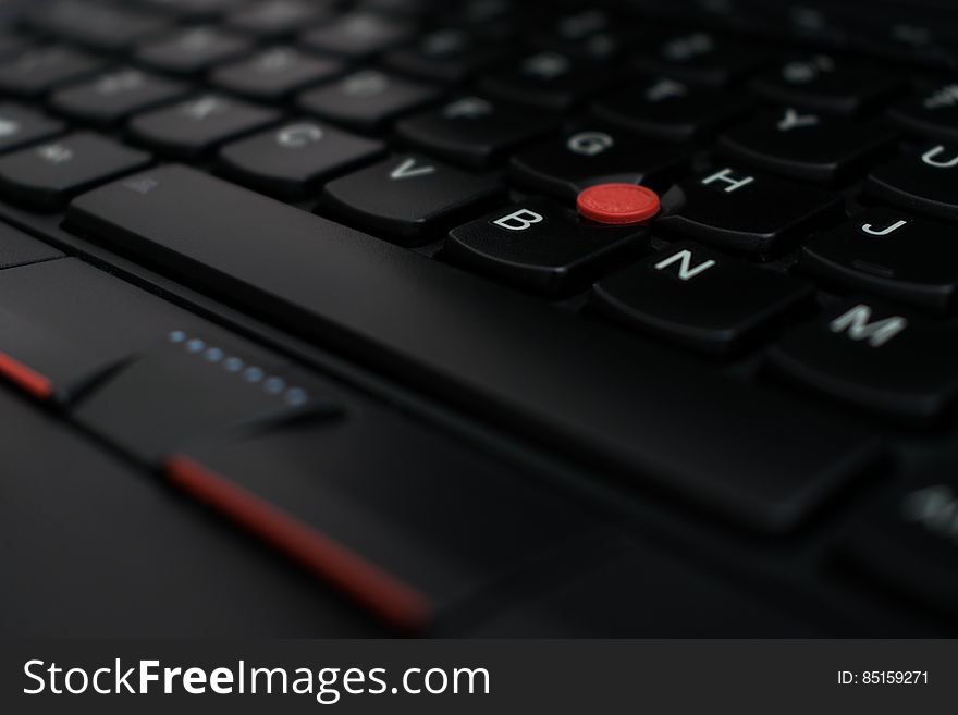 A close up of a laptop keyboard with a trackpoint mouse.