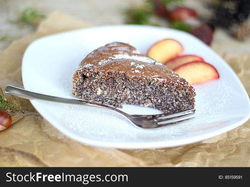 Piece of a baked chocolate dessert with fruit garnish and silver fork to the side on a white dish.