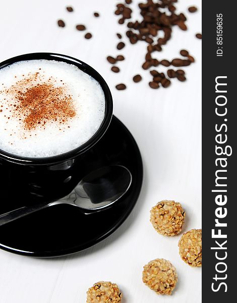 A close up of a cup of cappuccino with cinnamon on top, coffee beans and cookies beside.