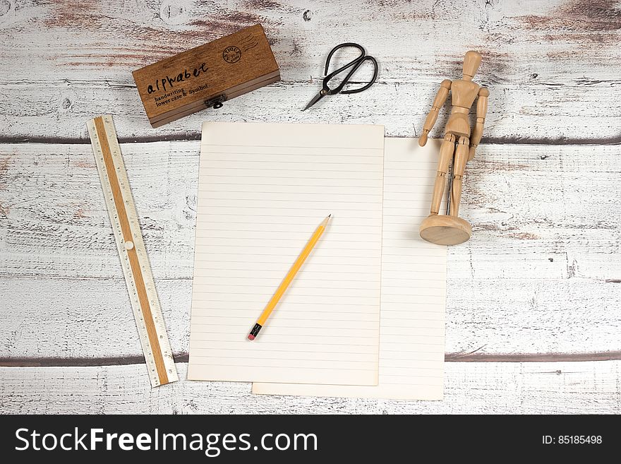 Blank page of paper with yellow pencil, ruler, scissors and wooden figurine on worn wooden slats. Blank page of paper with yellow pencil, ruler, scissors and wooden figurine on worn wooden slats.