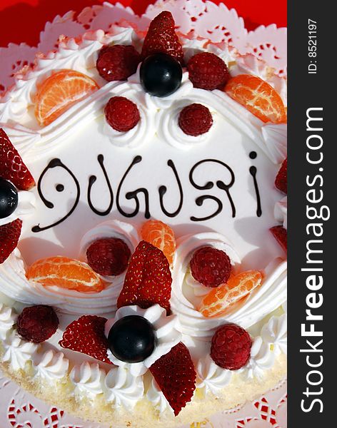 Birthday cake with Auguri, cream, strawberries, tangerine and grapes.
