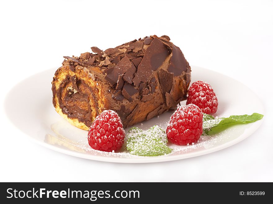 Miniature chocolate swiss roll cake served on a plate with mint leaves and raspberries on white background