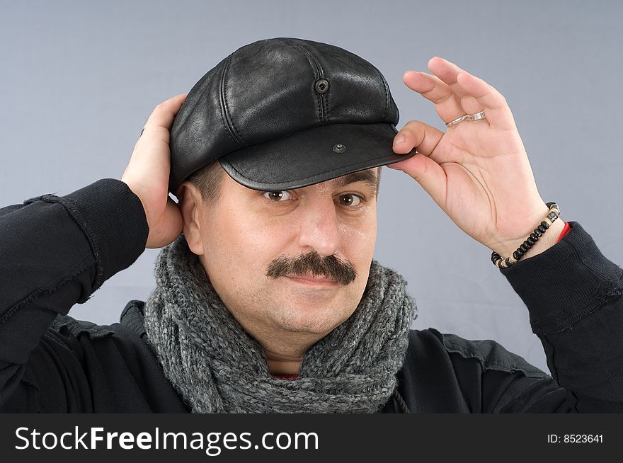 The moustached man in a black shirt and a cap is wrapped up by a scarf. The moustached man in a black shirt and a cap is wrapped up by a scarf.