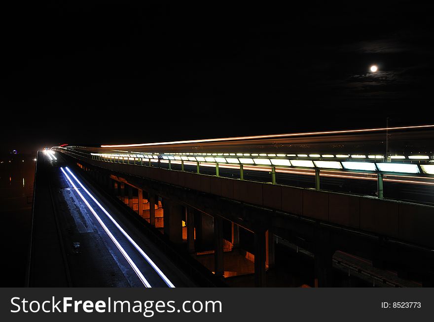 A subway-motor bridge with traces of a train and cars in the moonlit night. A subway-motor bridge with traces of a train and cars in the moonlit night