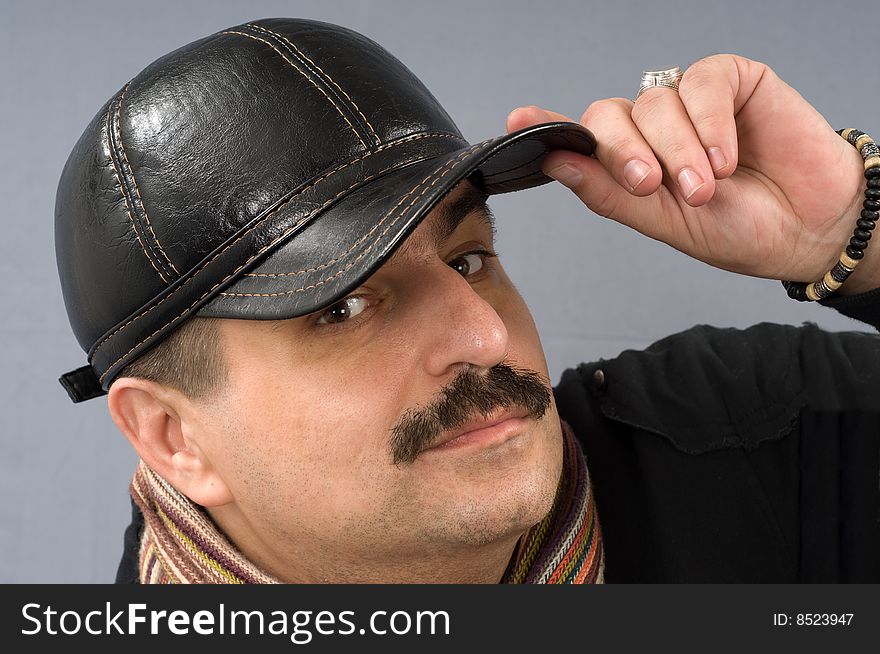 The moustached man in a black shirt and a cap is wrapped up by a scarf. The moustached man in a black shirt and a cap is wrapped up by a scarf.