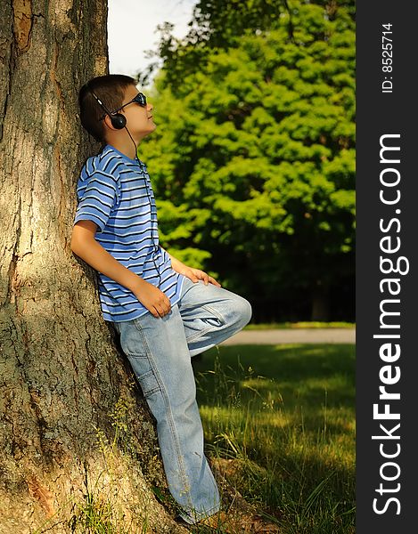 Boy listens to music having leant against a tree