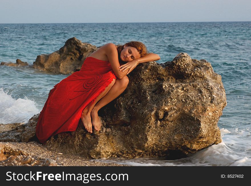 Young girl in orange dress lying on a rock on the sea shore, eyes closed. Young girl in orange dress lying on a rock on the sea shore, eyes closed