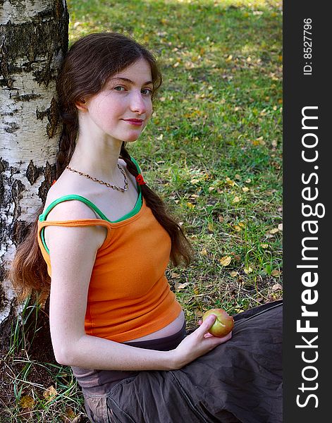 Pregnant girl sitting with an apple under a tree