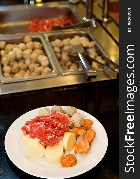 Raw food on a white plate in front of buffet table, ready to be boiled. Raw food on a white plate in front of buffet table, ready to be boiled