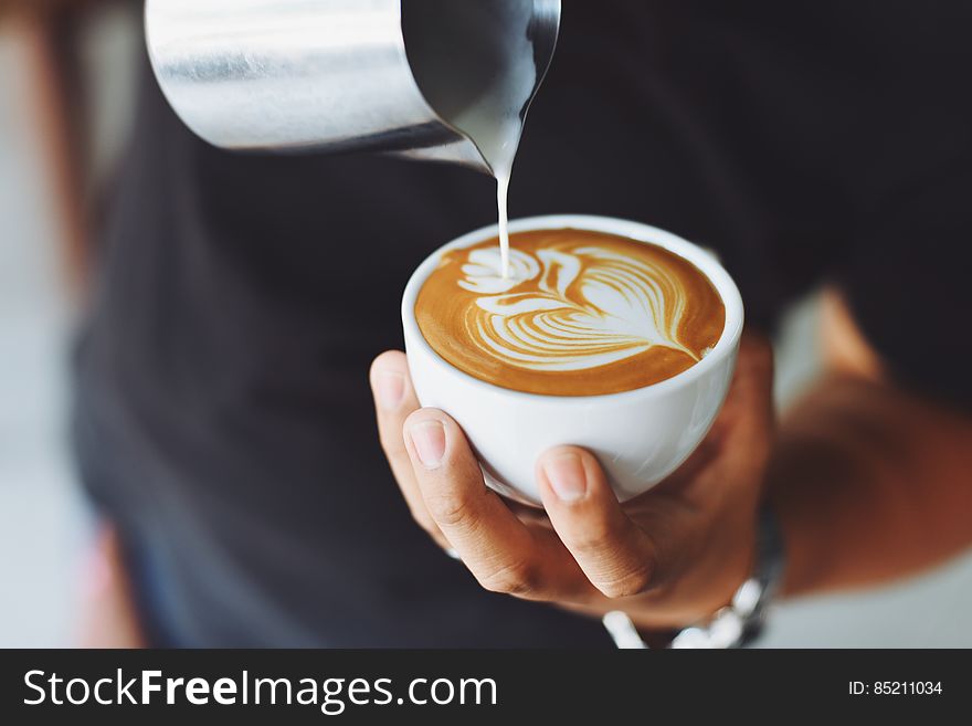 A barista pouring milk foam into a cup making latte art. A barista pouring milk foam into a cup making latte art.
