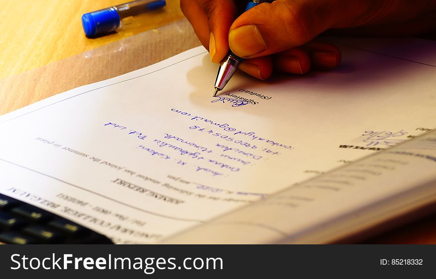 A close up of a hand signing a formal document with a pen. A close up of a hand signing a formal document with a pen.
