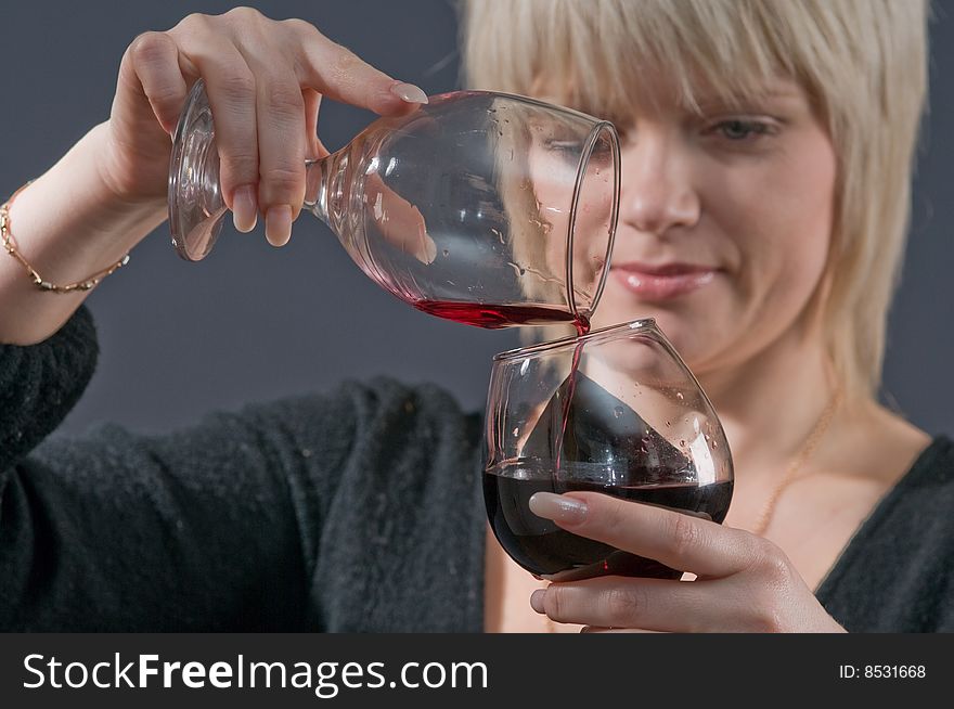 The blonde pours from a glass in a glass red wine. The blonde pours from a glass in a glass red wine.