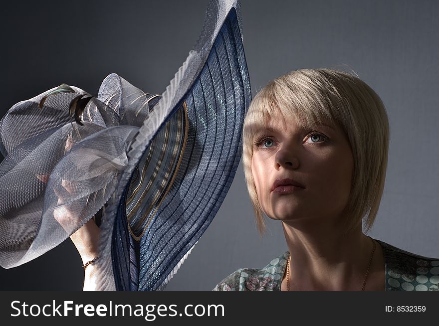 The woman the blonde in studio is covered with a hat from bright light. The woman the blonde in studio is covered with a hat from bright light.