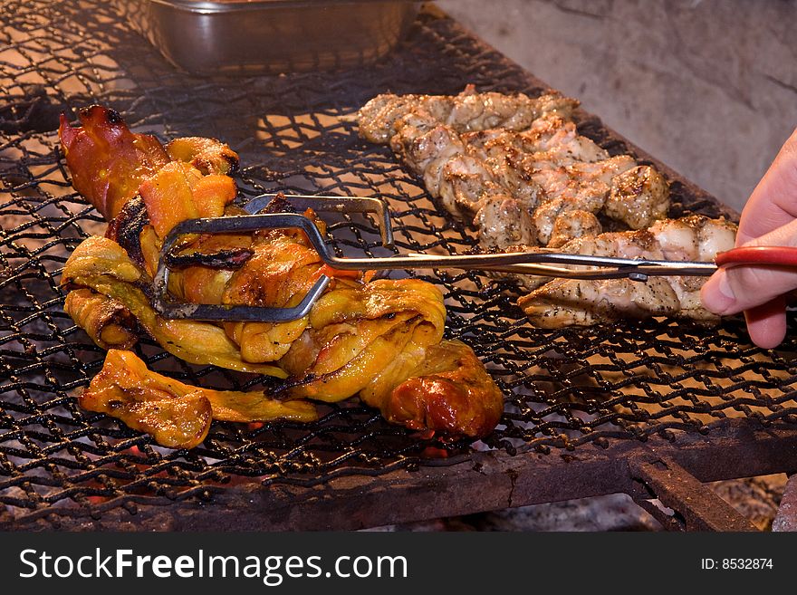 Pork fillet and chicken kebabs being grilled on an open fire and being turned by hand with tongs. Pork fillet and chicken kebabs being grilled on an open fire and being turned by hand with tongs