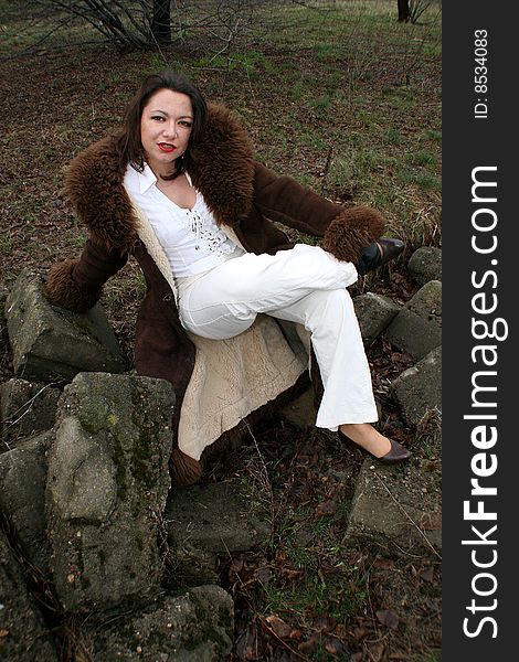 Smiling woman in sheepskin coat sitting on the rock.
