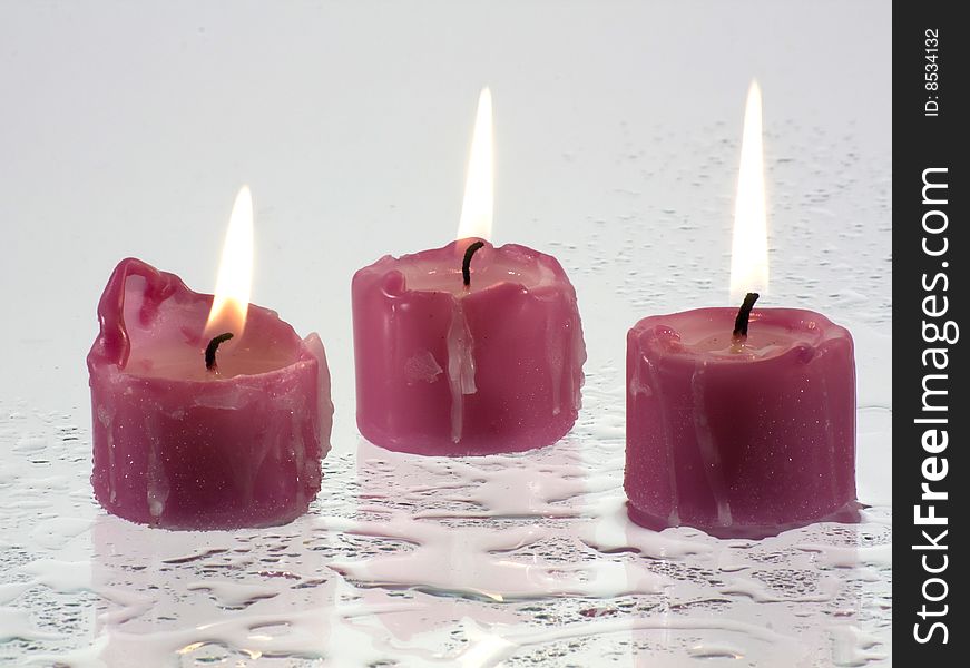 Candles, lit, standing on a wet surface that reflects light