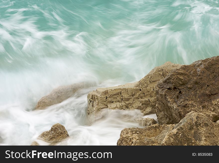 Green waves hitting rocky cliff