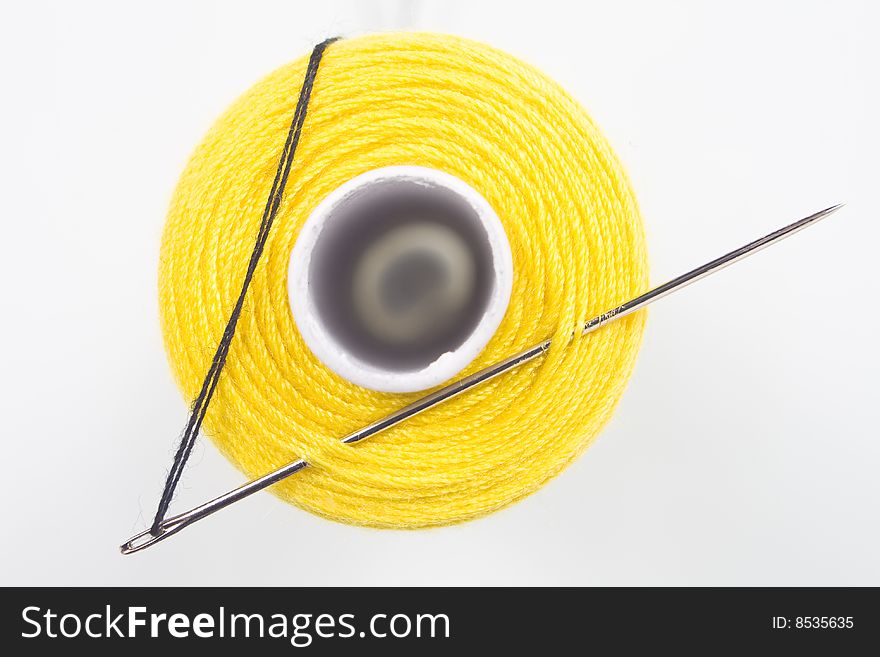 Close uyp of a yellow sewing spool with a needle