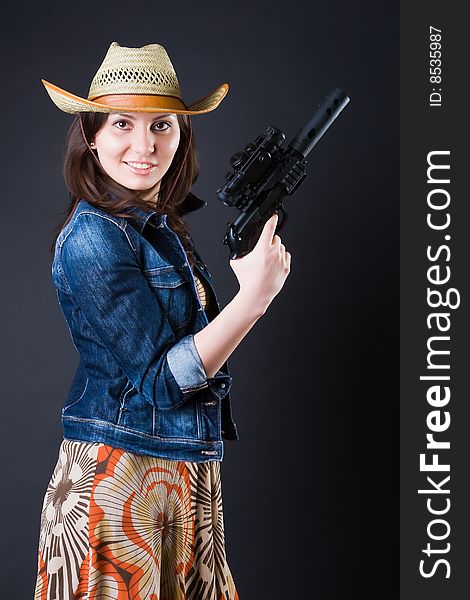 Girl in a cowboy's hat with the big pistol against a dark background. Girl in a cowboy's hat with the big pistol against a dark background