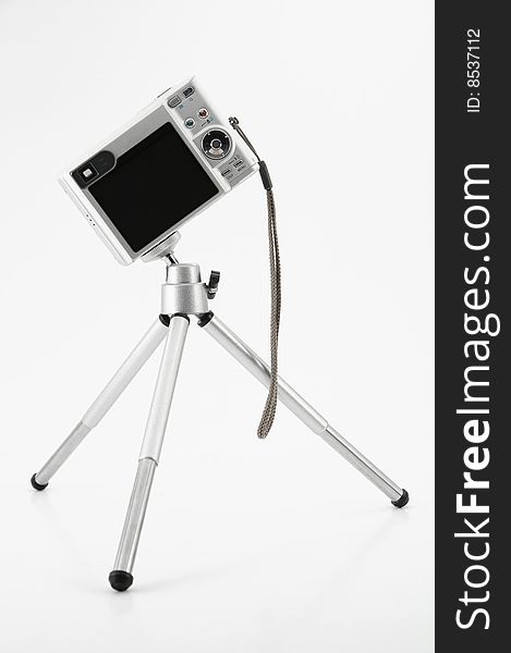 Small silver camera in dynamic angle on tripod against white background. Small silver camera in dynamic angle on tripod against white background