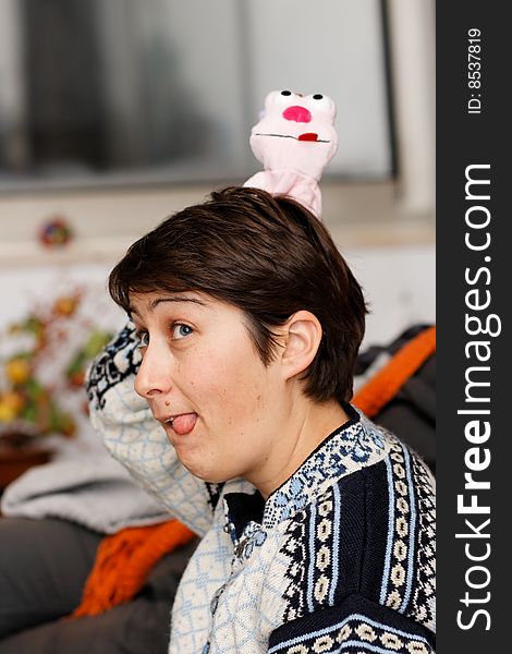 Young woman sticks out her tongue and has a doll on her head that sticks out her tongue too.
