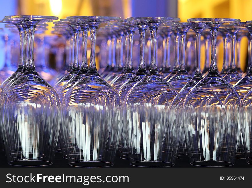 Rows of upturned wine glasses in a bar with colorful light reflection. Rows of upturned wine glasses in a bar with colorful light reflection.