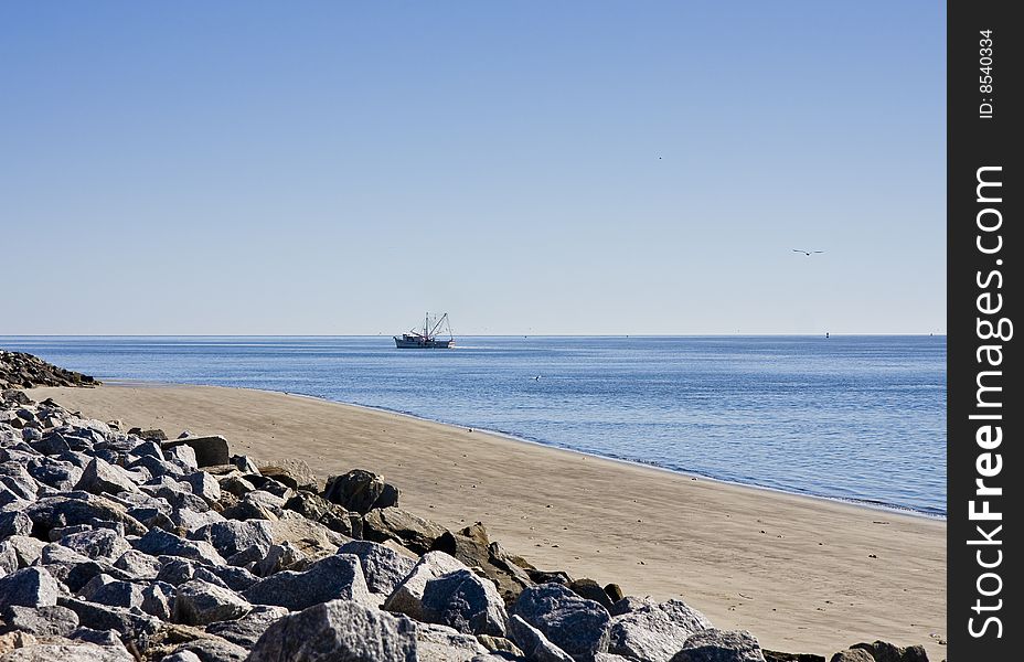 A shrimp boat off the coast of a rocky beach. A shrimp boat off the coast of a rocky beach