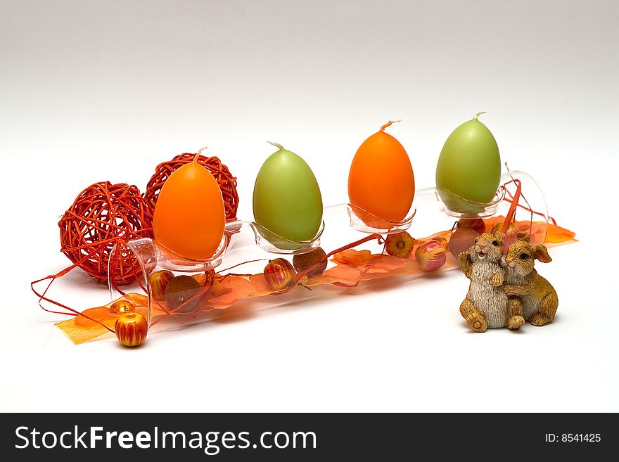 A composition of a glass tube with egg formed candles and a bit of spring feeling for easter, two bunnies in front and two red balls behind. A composition of a glass tube with egg formed candles and a bit of spring feeling for easter, two bunnies in front and two red balls behind