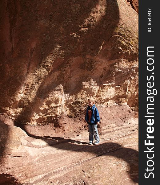 A color image of a young boy standing under a huge red rock cliff. A color image of a young boy standing under a huge red rock cliff.