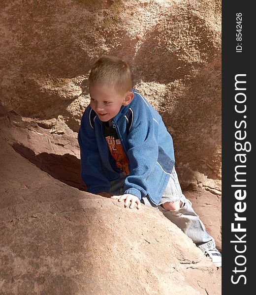 A color image of a young boy coming up and over some red rocks. A color image of a young boy coming up and over some red rocks.