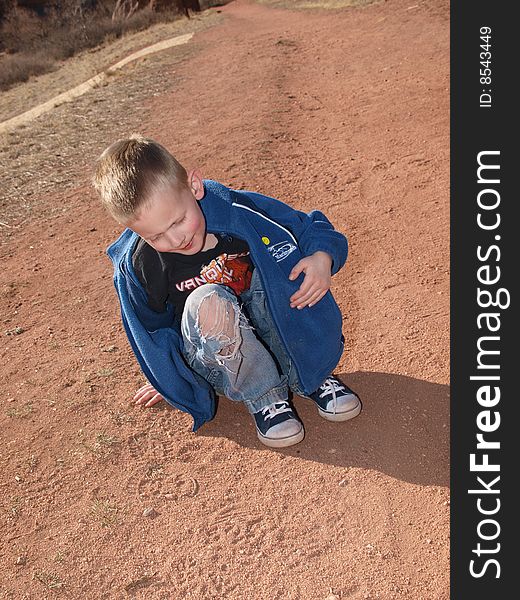 A color image of a youn boy sitting in the red dirt. A color image of a youn boy sitting in the red dirt.