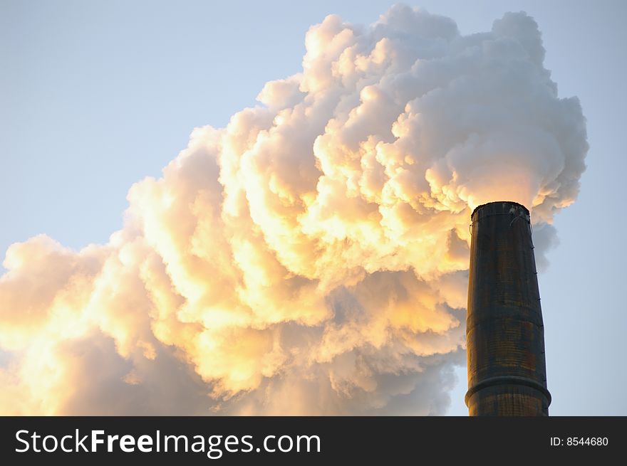 Close up shot of smoke billowing out of an industrial smoke stack and disappearing into a blue sky background.