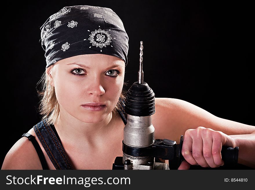 Severe young woman with a drill on black background
