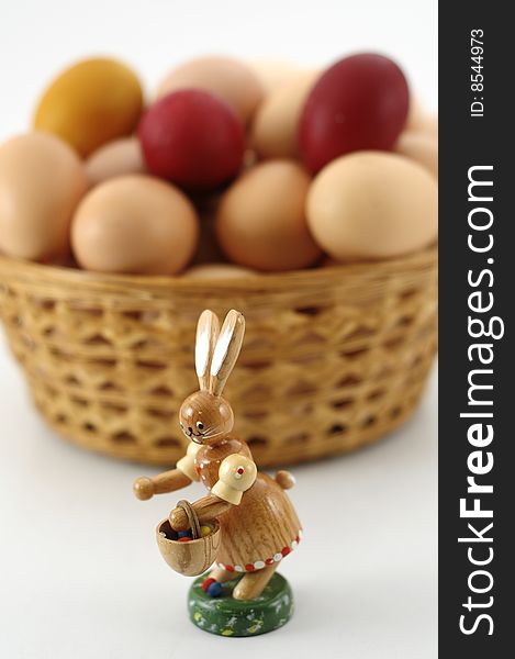 Wooden easter rabbit with basket and easter eggs in background, focus on rabbit