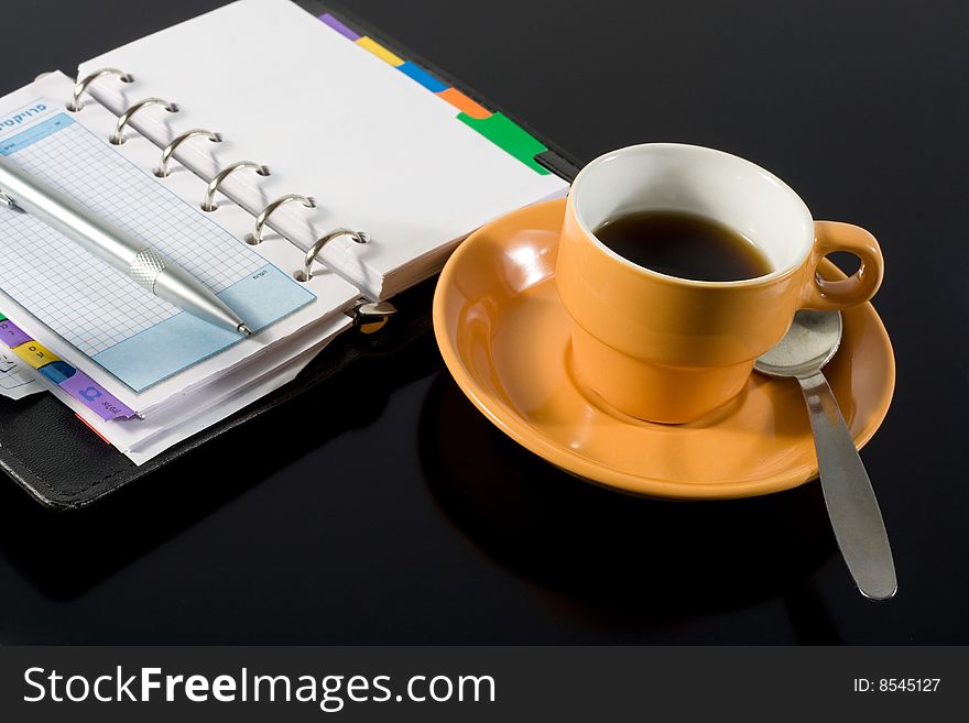 Orange coffee cup and a notepad on black background. Orange coffee cup and a notepad on black background