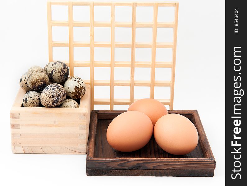 Zen inspired arrangement of quail and chicken eggs in wooden containers with square wooden grid in background. Zen inspired arrangement of quail and chicken eggs in wooden containers with square wooden grid in background