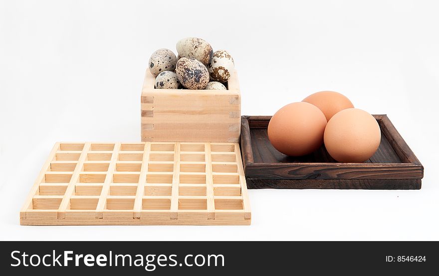 Zen inspired arrangement of quail and chicken eggs in wooden containers with square wooden grid on white background. Zen inspired arrangement of quail and chicken eggs in wooden containers with square wooden grid on white background